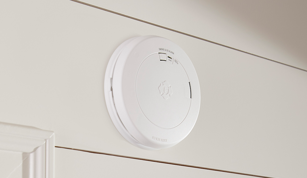 A white circular smoke detector mounted on a white paneled wall.